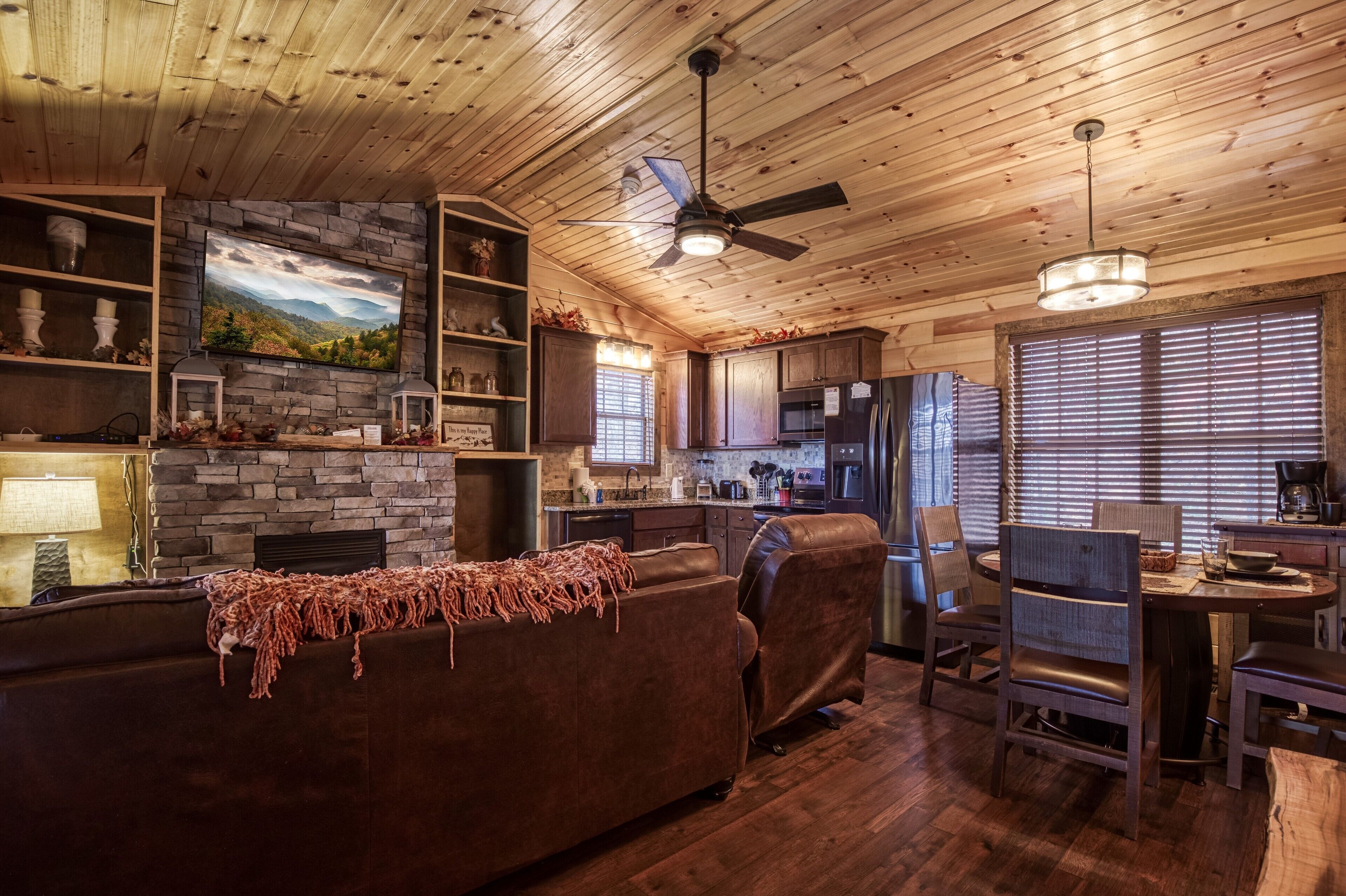 A cozy cabin interior with a stone fireplace, wooden ceiling, and a dining area.