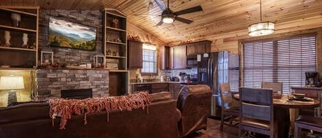 A cozy cabin interior with a stone fireplace, wooden ceiling, and a dining area.