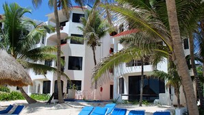 A beachfront hotel with multiple balconies, palm trees, and blue lounge chairs on the sand. - Akumal Paradise Private Studio - WiFi, Air Conditioning (Akumal, Riviera Maya)