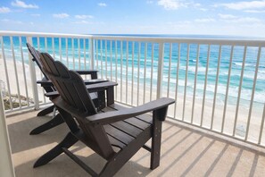 Ein Balkon mit zwei Adirondack-Stühlen mit Blick auf einen Strand mit klarem, blauem Wasser und einer weißen Brüstung.