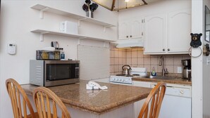A compact kitchen with a granite countertop, white cabinets, a microwave, a stove, and wooden chairs. - (B210) Loft Condominiums (Yosemite National Park)