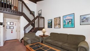 A living room with a wooden coffee table, two green sofas, a lamp, and framed pictures on the wall. - (B210) Loft Condominiums (Yosemite National Park)