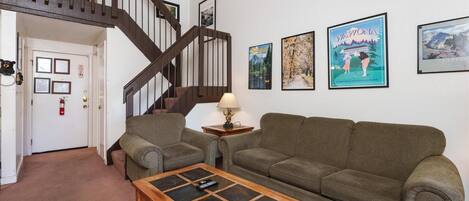 A living room with a wooden coffee table, two green sofas, a lamp, and framed pictures on the wall.