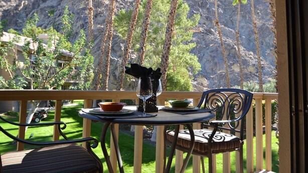 A balcony with a table set for two, overlooking a mountainous landscape with palm trees.
