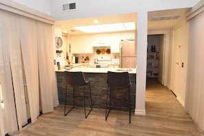 A modern kitchen with a central island, two bar stools, and a stone backsplash.