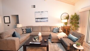 A living room with a sectional sofa, a patterned armchair, a coffee table, a lamp, and a painting on the wall.
