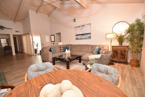 A spacious living room with a wooden coffee table, two patterned armchairs, a sofa, and a dining table with white spherical decorations.