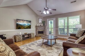 A living room with a fireplace, a ceiling fan, a large window, and a sofa.