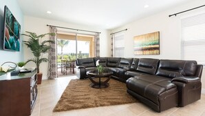 Ein modernes Wohnzimmer mit einer Eckcouch, einem Couchtisch und einem Fernseher. Ein großes Fenster mit Vorhängen, eine Pflanze und ein Bild an der Wand sind ebenfalls zu sehen.