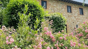 A stone building with a tiled roof, surrounded by lush greenery and flowering plants. - Beautiful house near San Gimignano in Tuscany with views, pool,garden, A/C, WiFi (Gambassi Terme, FI)