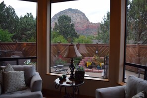A room with a large window offering a view of a mountain and greenery. There is a round table with a lamp and decorative items. - UPSCALE PRIVATE HOME, SPECTACULAR VIEWS, WALK TO TRAILS, HUGE DECK QUIET!!!! (Sedona)