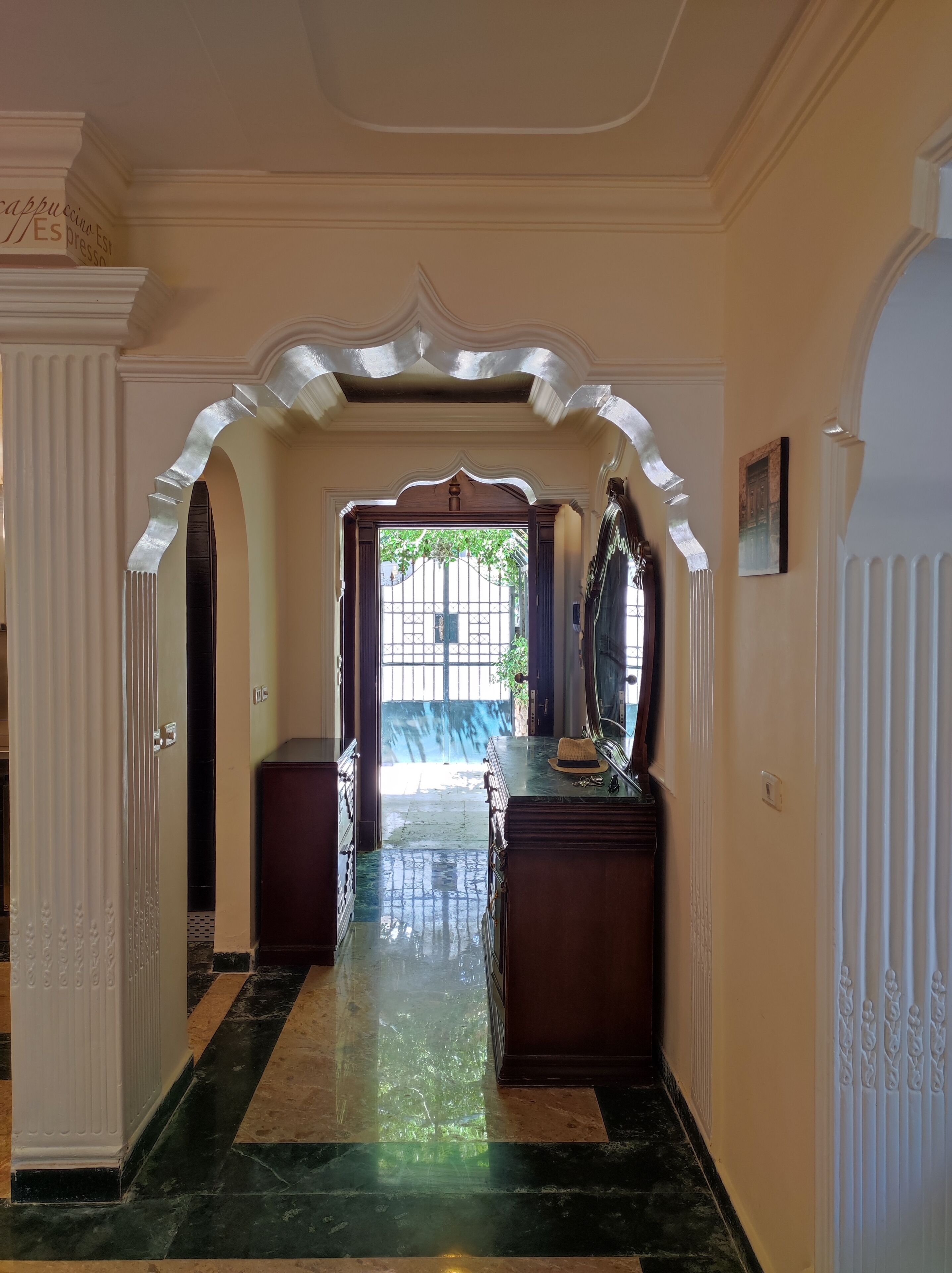 A hallway with a marble floor, a wooden cabinet, and a decorative archway.