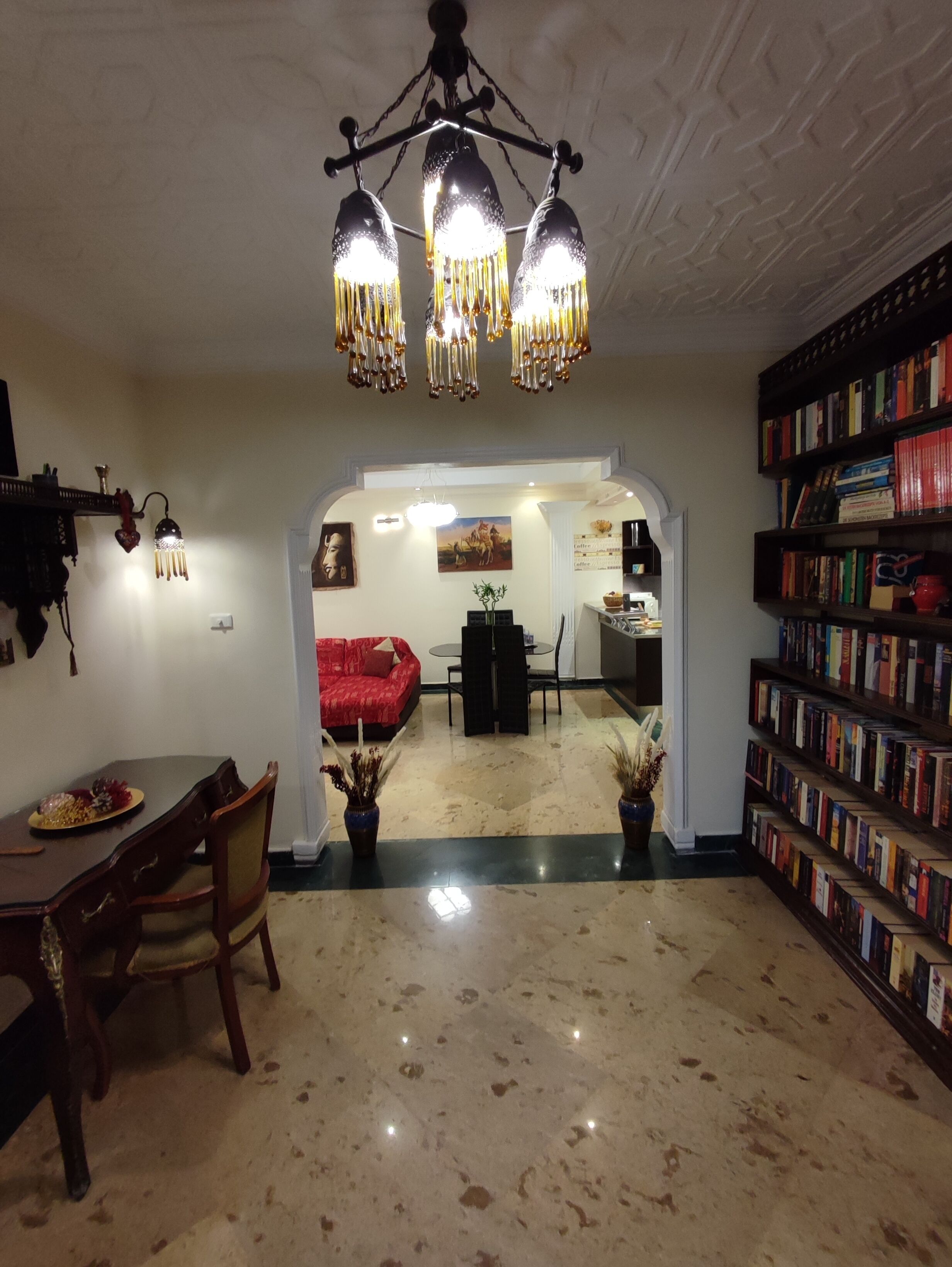 Un vaste espace de vie comprenant une table à manger, des chaises, un canapé rouge, une bibliothèque et, au fond, une cuisine.