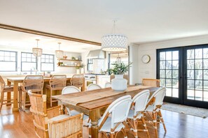 A spacious kitchen with a large dining table, wicker chairs, and a hanging light fixture. - Gorgeous Home 2 Min Walk to Beach! (Harwich Port)