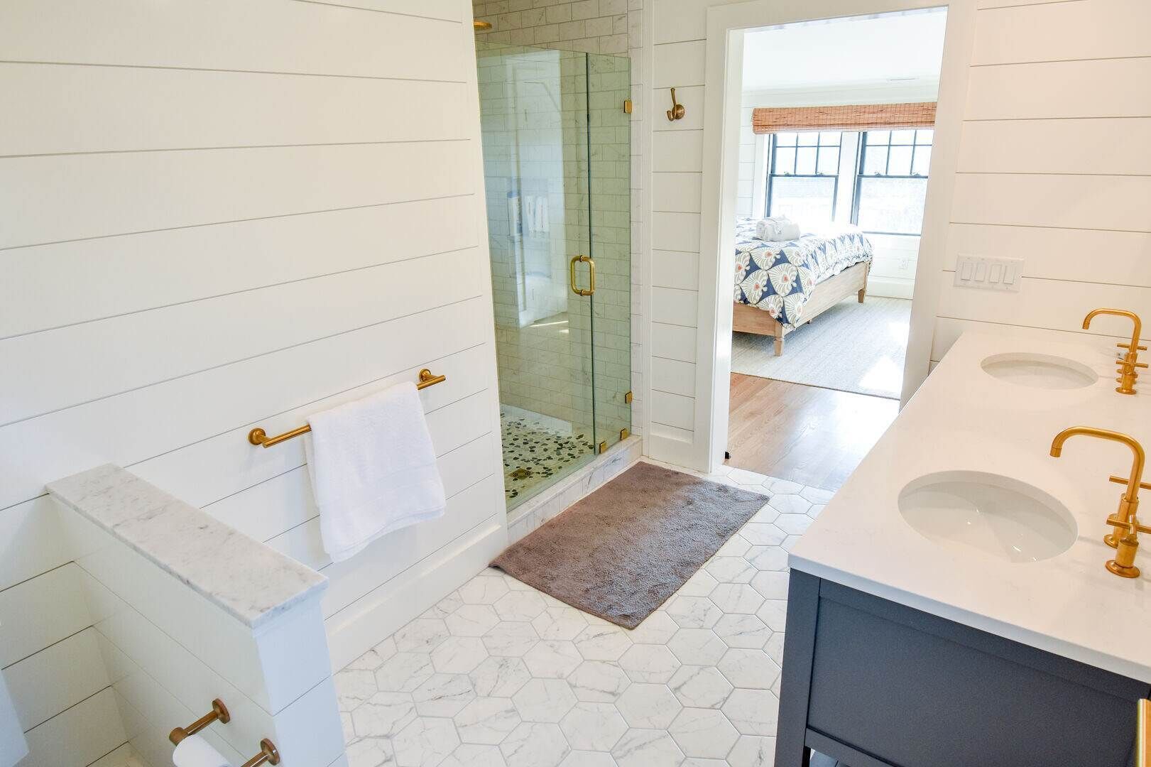 A bathroom with a shower, two sinks, and a visible bedroom with a bed.