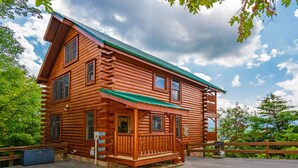 A log cabin with a green roof, a porch, and a fenced driveway. - 🐾Paradise Point 🏔️LeConte Views, Hot Tub, Resort Pool! Near Attractions! (Sevierville)