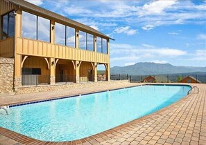 A swimming pool with a stone deck, a wooden building with large windows, and a mountainous backdrop. - ParadisePoint: SpectacularView, PetFriendly, HotTub, Wifi, ResortPool! Near Attractions! (Sevierville)