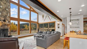 Un salón amplio con un sofá seccional gris grande, una chimenea y una zona de cocina con una isla de madera y taburetes de bar.