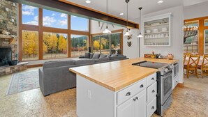 Una cocina moderna con una isla central, horno empotrado y grandes ventanales con vistas a árboles otoñales.