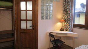 A room with a wooden door, a desk with a chair, a window with patterned curtains, and a bed with a white blanket. - Podere la Piana-Cedro (fivizzano)