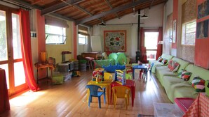 A spacious living area with a high wooden ceiling, a green sofa with colorful cushions, a wooden floor, and a large window with red curtains. - Podere la Piana-Cedro (fivizzano)
