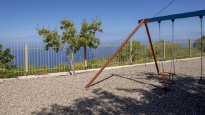 A swing set in a park with a clear view of the sea in the background.