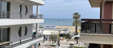 A multi-story hotel with balconies, a view of the beach, and a parking area with cars.