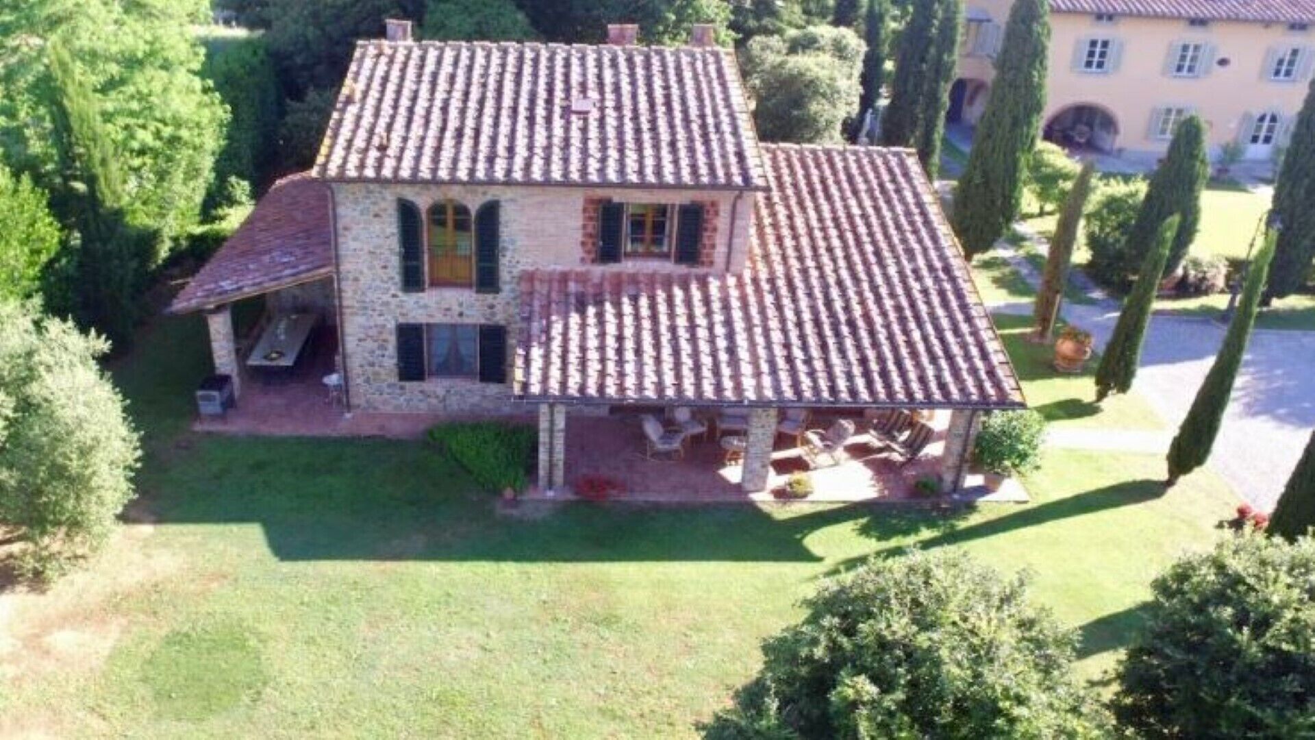 A two-story stone house with a tiled roof, a covered patio, and a well-maintained lawn.