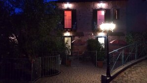 Un bâtiment en pierre avec deux fenêtres illuminées et une cour dallée.