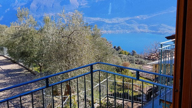Un escalier avec des rampes bleues menant à un balcon d’où l’on peut admirer un paysage montagneux et une étendue d  ’eau.