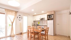 Una cocina moderna con armarios de madera, un microondas y un refrigerador. Hay una mesa de comedor con sillas y un reloj en la pared.