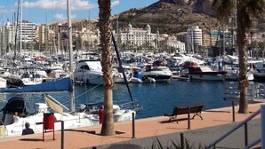 Una marina con barcos amarrados, palmeras y una colina rocosa al fondo.