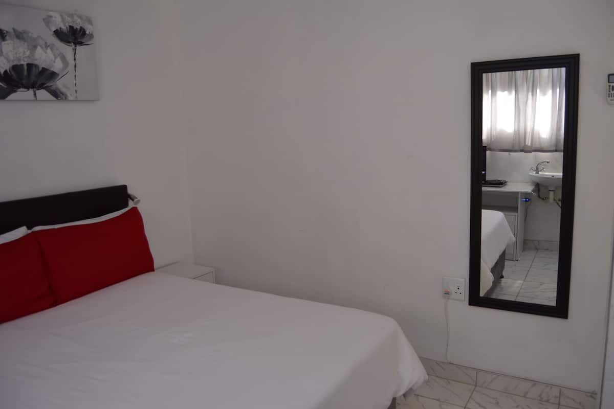 A hotel room with a bed, a mirror, a wall-mounted artwork, and a bathroom visible through the mirror.