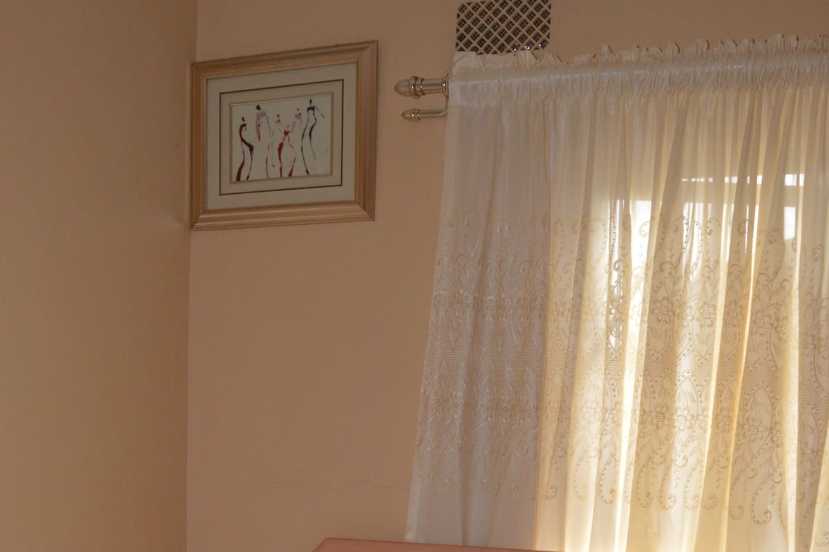 A neatly made bed with a patterned bedspread, a pillow with a square pattern, and a wooden nightstand with a drawer.