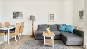 Ein modernes Wohnzimmer mit einem grauen Sofa, Korbstühlen, einem kleinen Tisch mit einer Vase und schwarzen und weißen gerahmten Fotos an den Wänden.