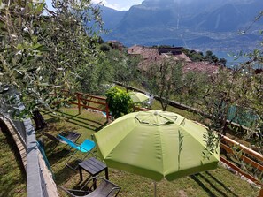 A terrace with outdoor furniture, a green umbrella, and a view of a mountainous landscape. - Ulivi sul Garda apartment 1  017189-CNI-00293 (Tremosine)
