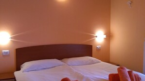 Et hotelværelse med en stor seng, hvide sengetøj og to sammenrullede håndklæder på sengen. Der er vægmonterede lamper over sengen.