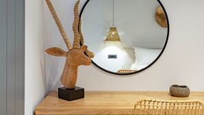 A wooden sculpture of an animal head on a wooden table, a round mirror with a black frame, and a hanging light fixture. - Lemon Suites Santorini (Santorini)