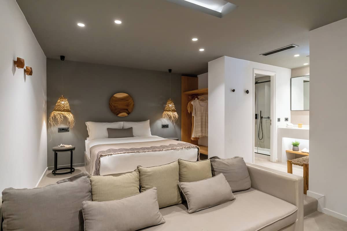 A modern bedroom with a large bed, bedside lamps, a wooden wardrobe, and a small table with a plant.