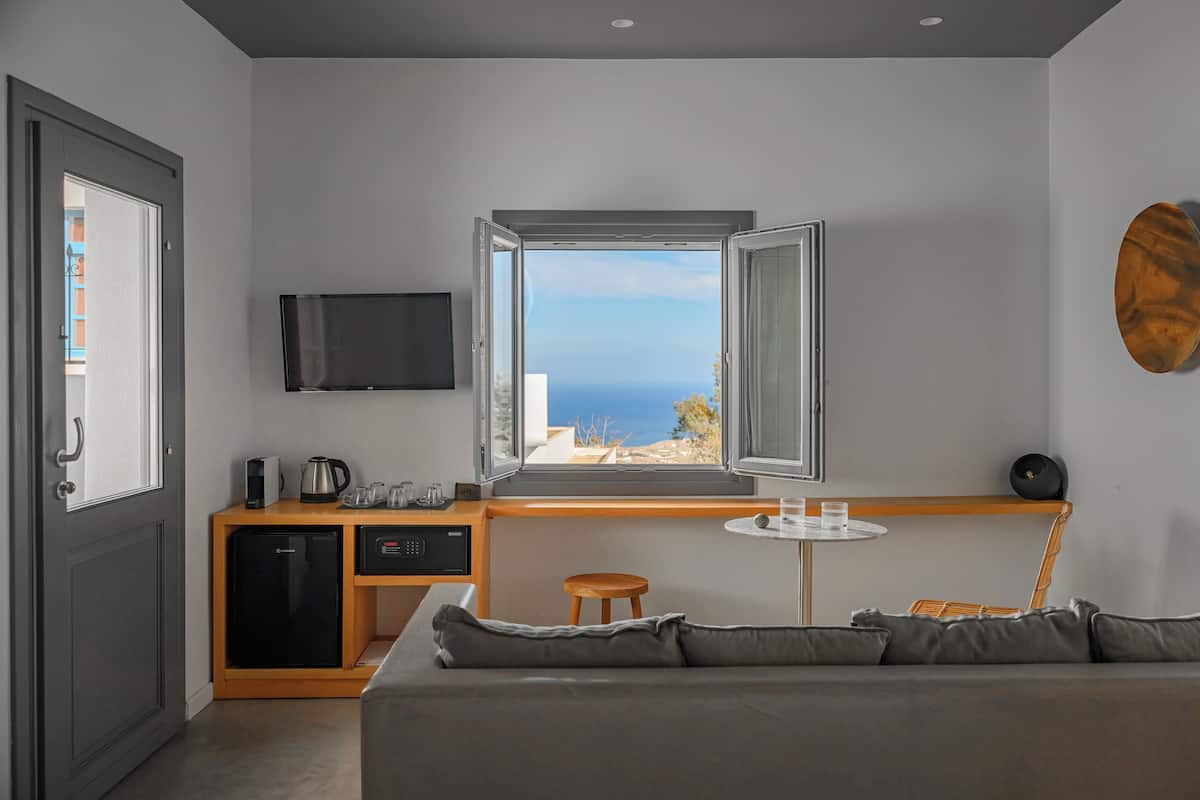 A modern room with a large window, a sofa, a small table, a TV, and a kitchenette.