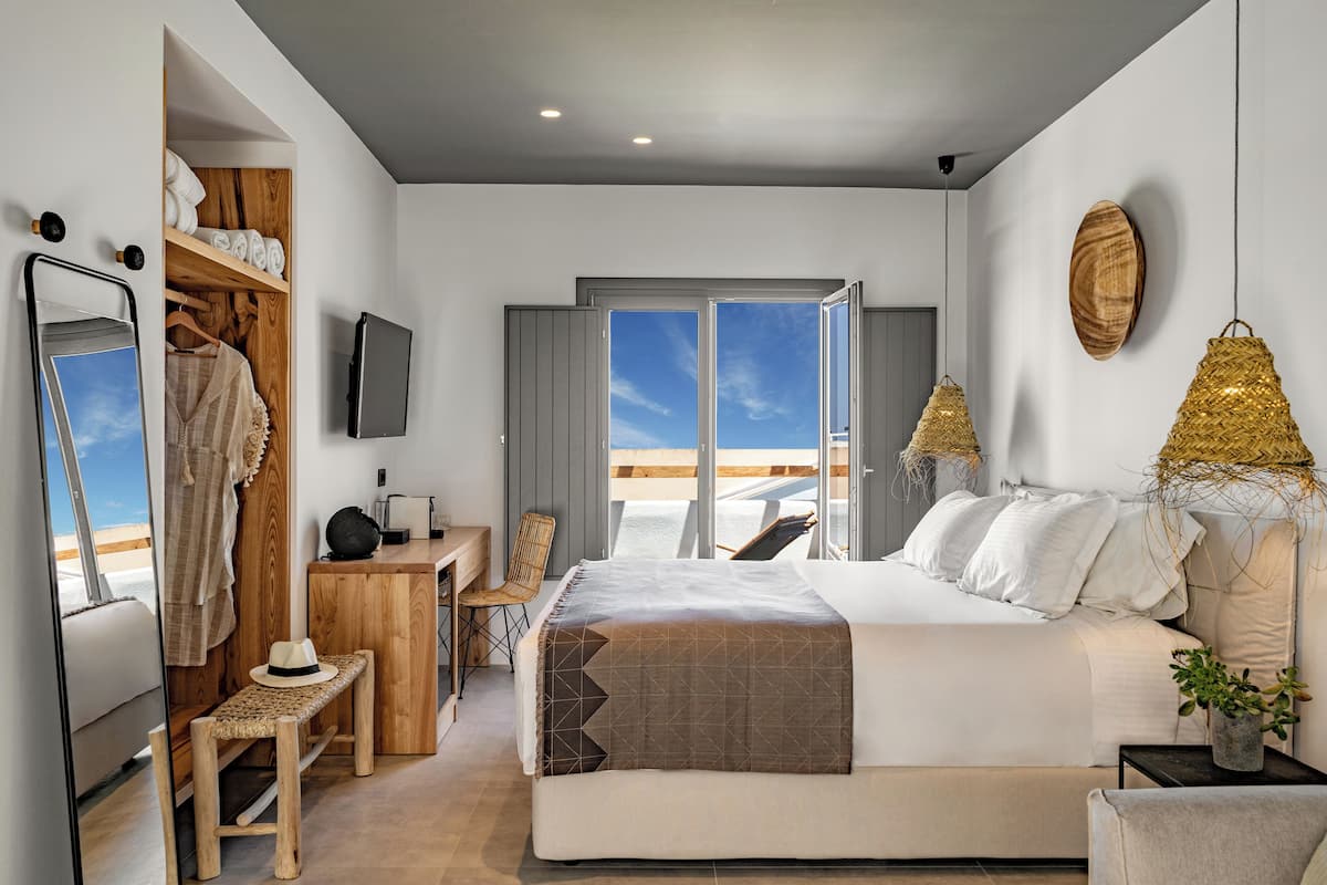 A modern bedroom with a large bed, a wooden desk, a chair, a small table, and a TV.