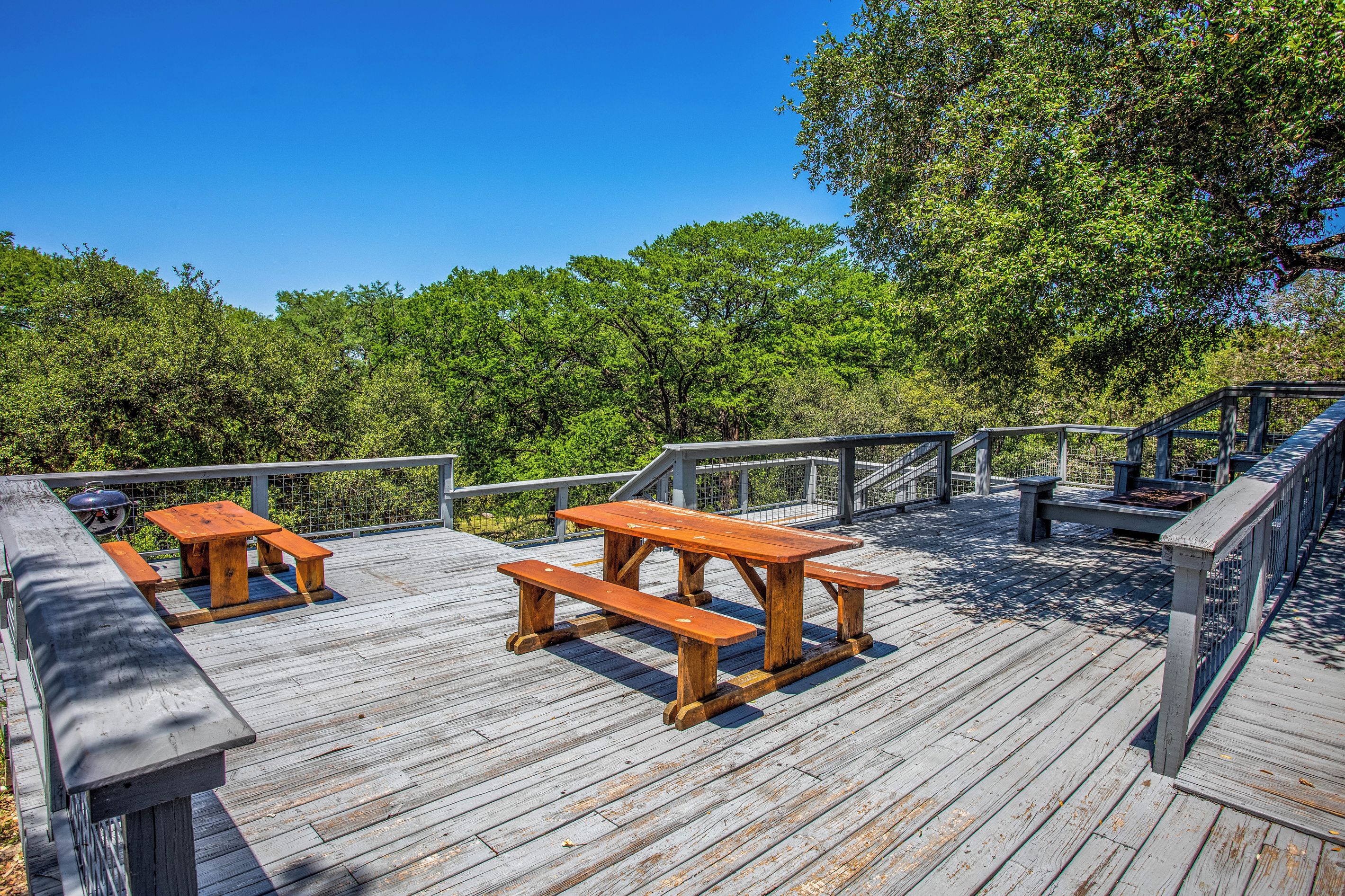A wooden deck with picnic tables and a barbecue grill.