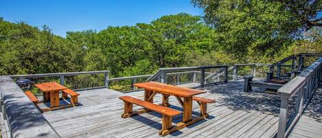 A wooden deck with picnic tables and a barbecue grill.