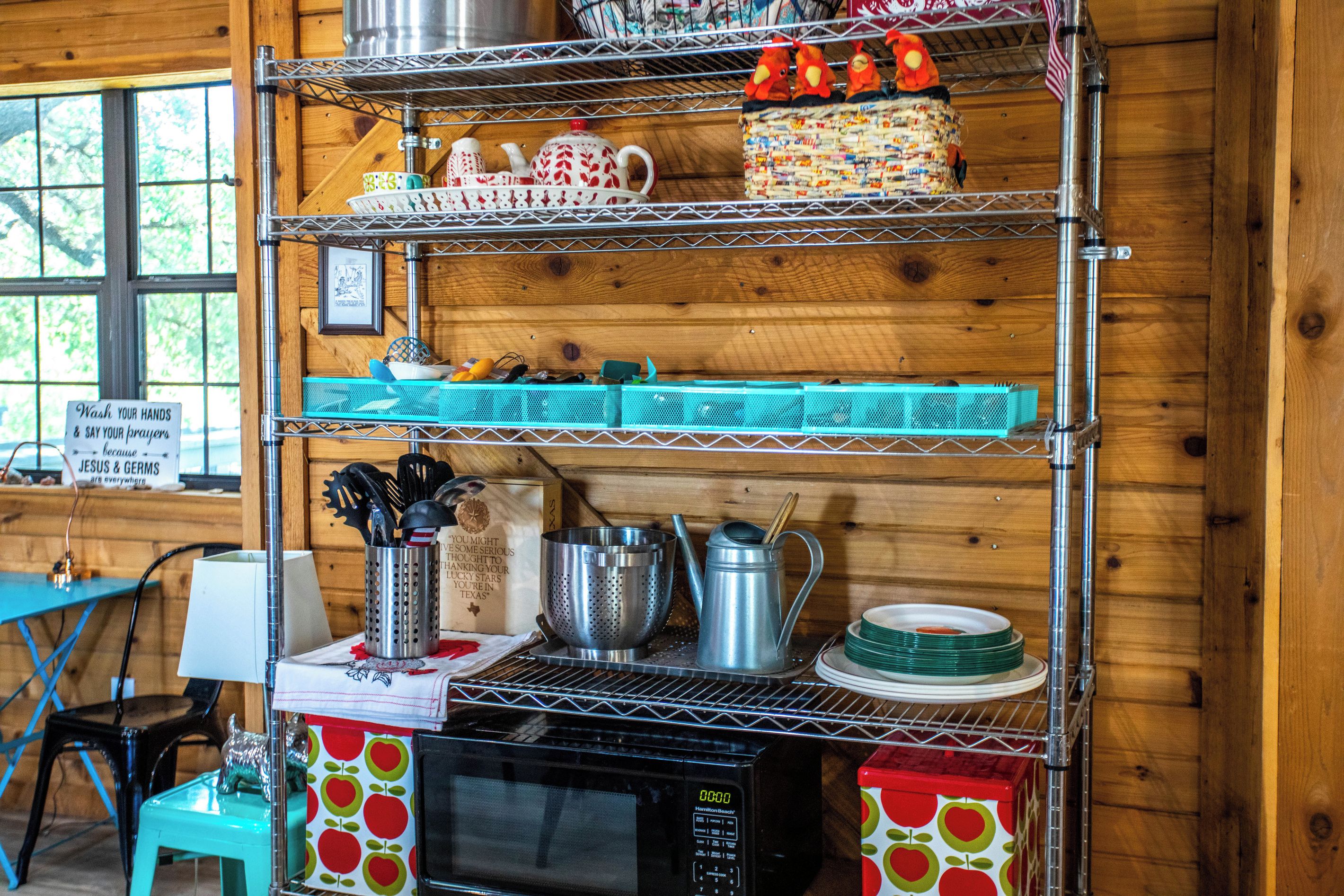 A kitchen with a microwave, a coffee maker, and various utensils on shelves.