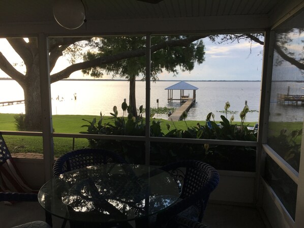 A covered patio with a glass table and wicker chairs, overlooking a lake with a dock and gazebo. - Lake June Zen Retreat (Lake Placid)
