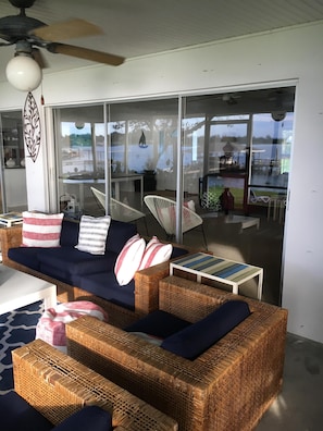 A wicker sofa with cushions, a small table, and a ceiling fan in a room with large windows. - Lake June Zen Retreat (Lake Placid)