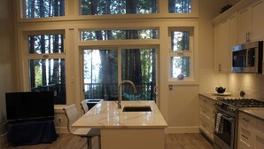 A modern kitchen with large windows, a built-in island, stainless steel appliances, and a flat-screen TV.