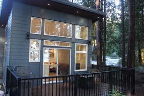 A modern cabin with large windows, a deck, and a view of the surrounding forest. - Coastal Retreat on the Sunshine Coast BC (Sechelt)