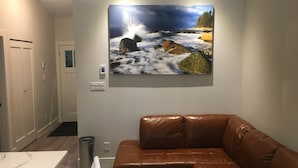 A modern bathroom with a marble countertop, a brown leather bench, and a large painting of a rocky coastline.