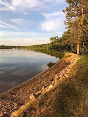 Vista para o lago com margem rochosa, árvores e céu claro.